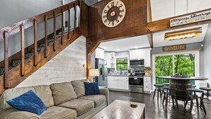 A spacious living area with a wooden staircase, a kitchen in the background, and a view of the outdoors. - Winter Retreat, Hot Tub, Fire Pit, 7min to Ellijay. 16min to Blue Ridge (Ellijay)