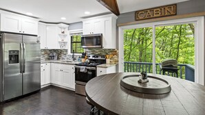A modern kitchen with white cabinets, stainless steel appliances, and a large island. A 'CABIN' sign is visible above a window with a view of trees. - Winter Retreat, Hot Tub, Fire Pit, 7min to Ellijay. 16min to Blue Ridge (Ellijay)