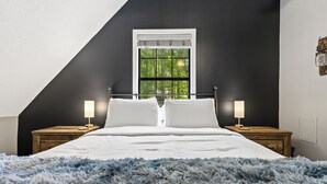 A bedroom with a large bed, two bedside tables, a window with a view of trees, and a sloped ceiling. - Winter Retreat, Hot Tub, Fire Pit, 7min to Ellijay. 16min to Blue Ridge (Ellijay)