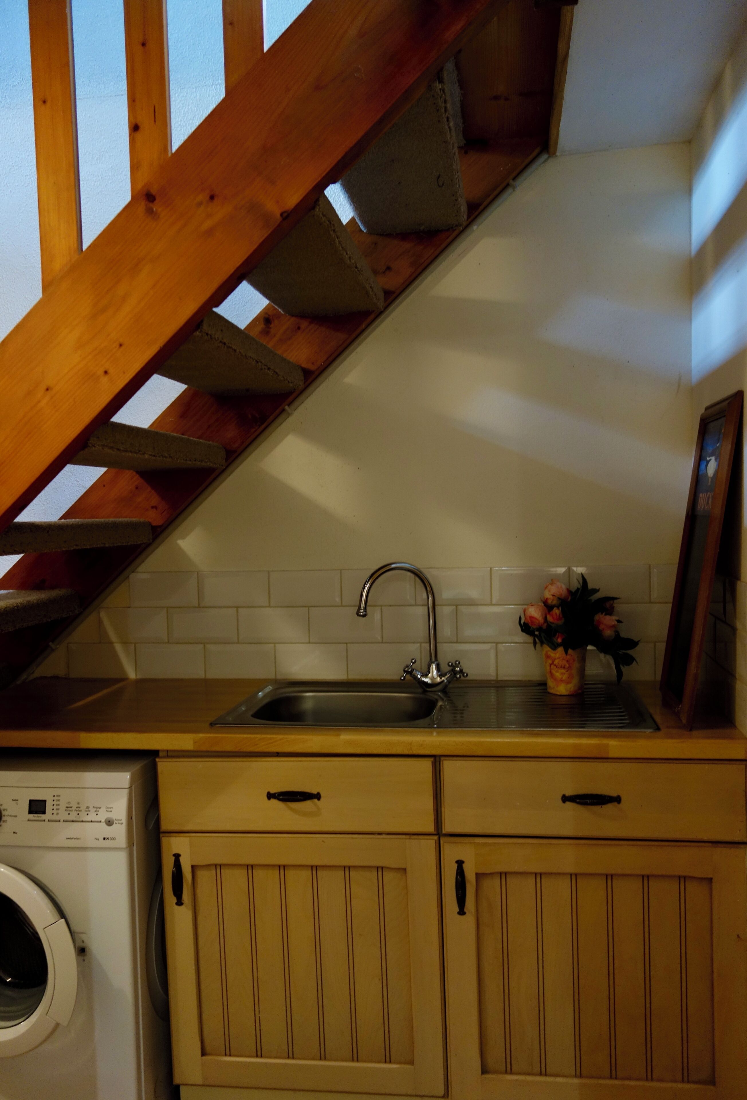 Een keuken met een houten trap, een wasmachine en een spoelbak.