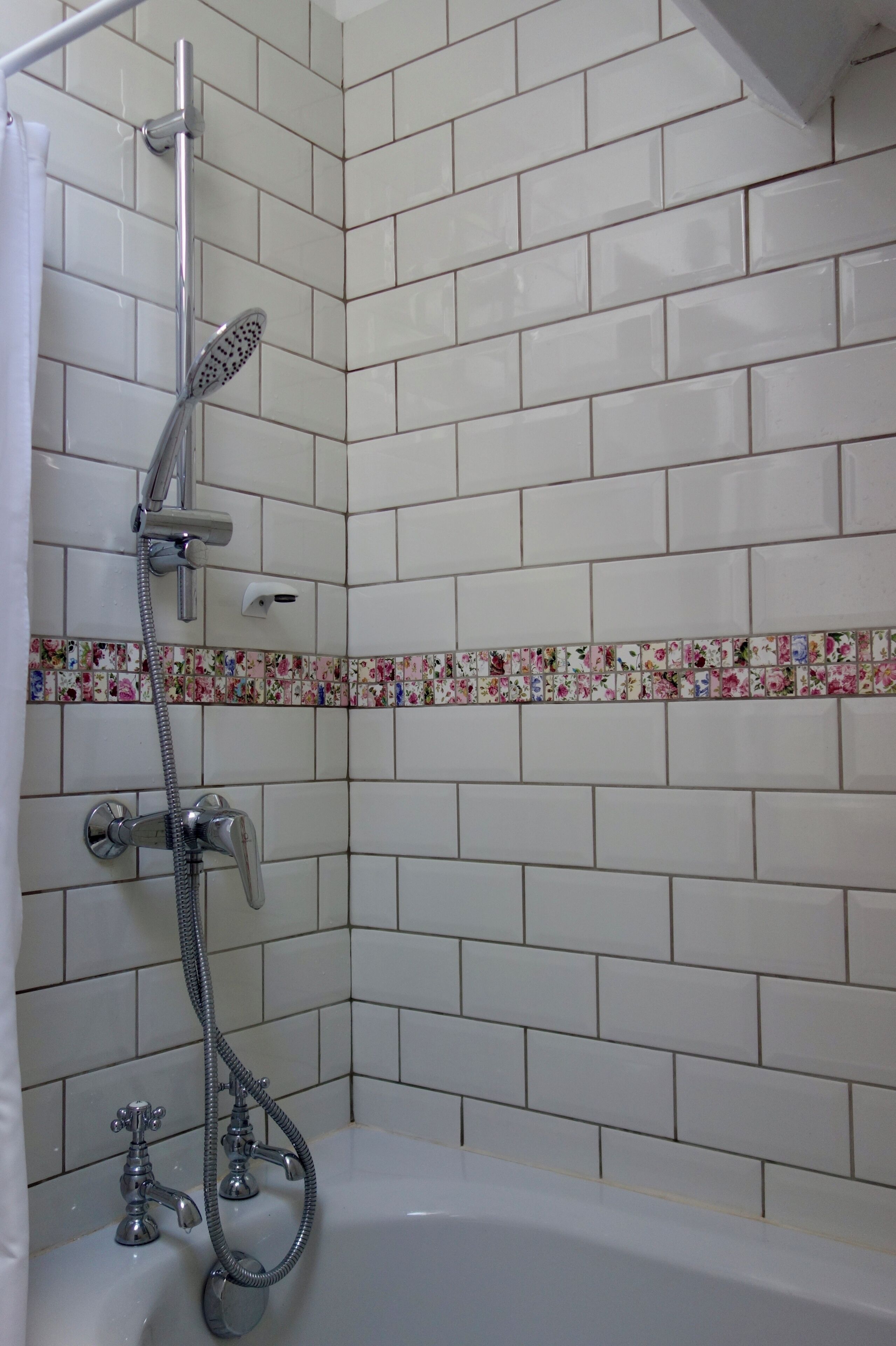 A bathroom with white tiles, a shower with a handheld showerhead, and a bathtub.