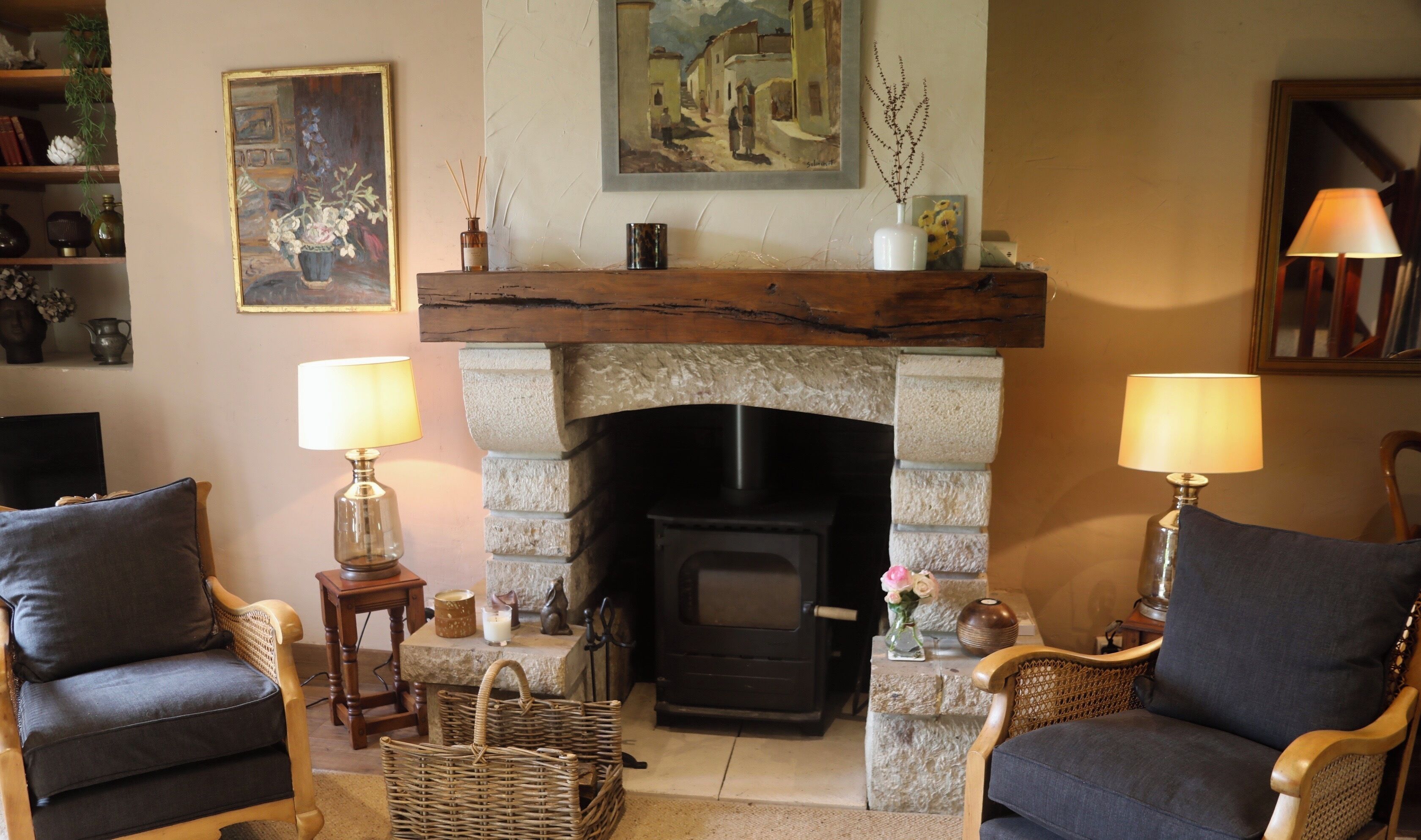 A cozy living room with a stone fireplace, two armchairs, a small table with a candle, and a painting above the fireplace.