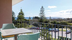 Un balcon avec une table et des chaises, donnant sur un parking et offrant une vue sur la mer.