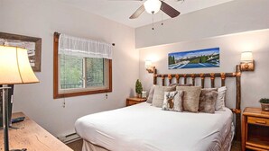 A bedroom with a large bed, a window with a view, a painting on the wall, and two bedside tables. - Lionshead Village 2 Bedroom With Pool, Walk to Slopes! (Vail)