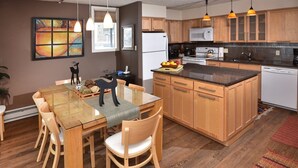 A modern kitchen with wooden cabinets, a central island, and pendant lighting. - Lionshead Village 2 Bedroom With Pool, Walk to Slopes! (Vail)