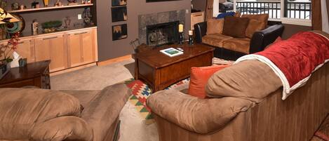 Una sala de estar acogedora con chimenea, un conjunto de sofás, una mesa de centro y una estantería.