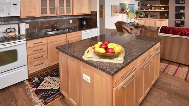 A modern kitchen with wooden cabinets, a granite countertop, and a central island with a bowl of fruit. - Lionshead Village 2 Bedroom With Pool, Walk to Slopes! (Vail)