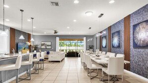 Un hall d’hôtel moderne avec un long comptoir d’accueil, un espace salon avec un canapé et des fauteuils, et un coin repas avec une longue table et des chaises.
