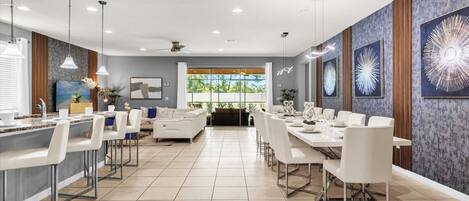 Un hall d’hôtel moderne avec un long comptoir d’accueil, un espace salon avec un canapé et des fauteuils, et un coin repas avec une longue table et des chaises.