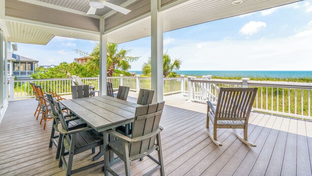 A covered outdoor deck with a table and chairs, overlooking a beach. - The Great Escape: Oceanfront 6BR Home (Georgetown)