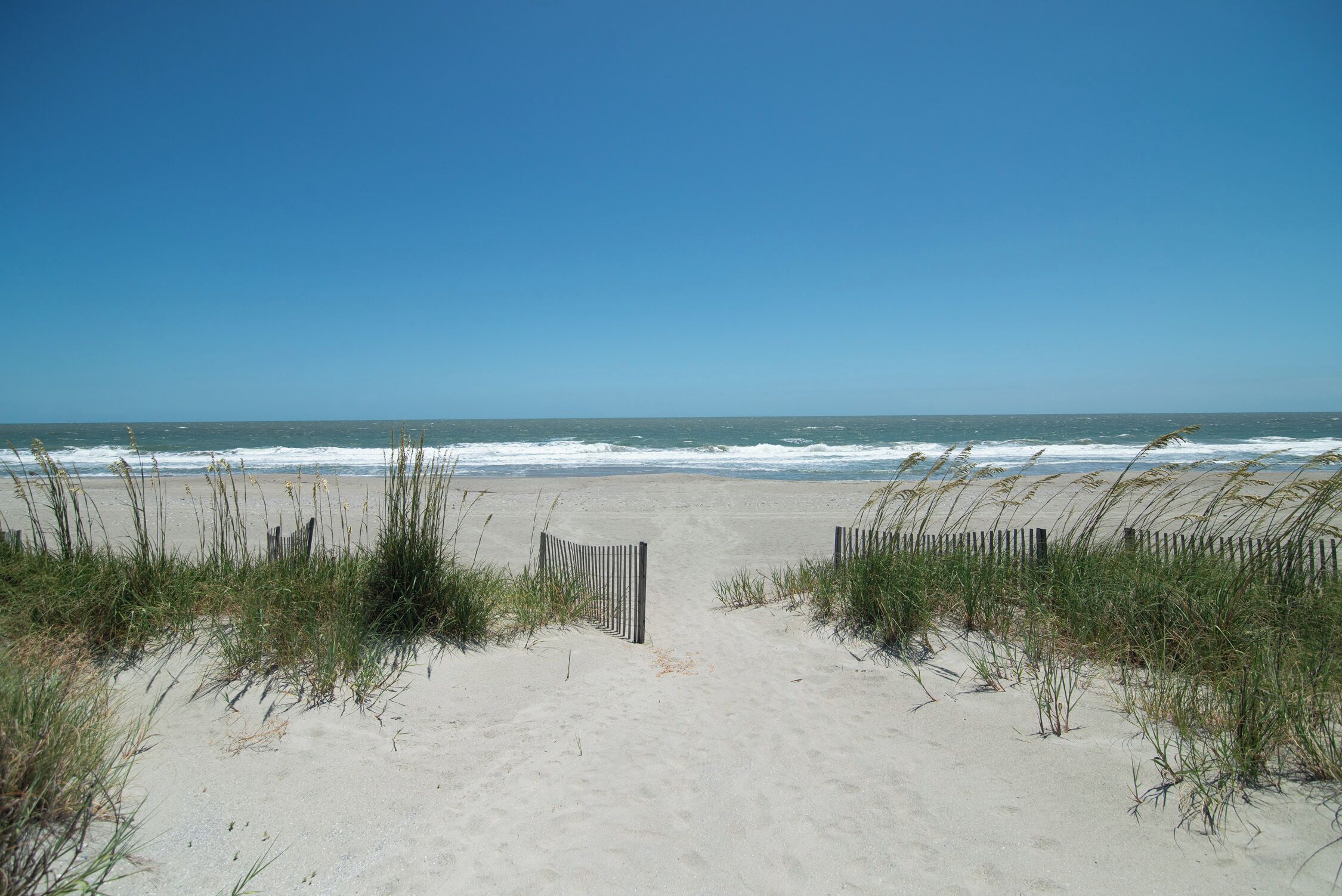 A sandy beach with a wooden fence leading to the ocean.
