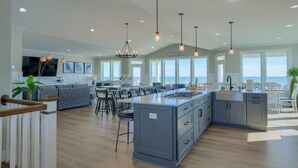 A spacious kitchen with a central island, bar stools, and a dining area with a view of the ocean. - Paradise #169 - Mini-Resort, Private Pool & Hot Tub, Sleeps 38 (North Topsail Beach)