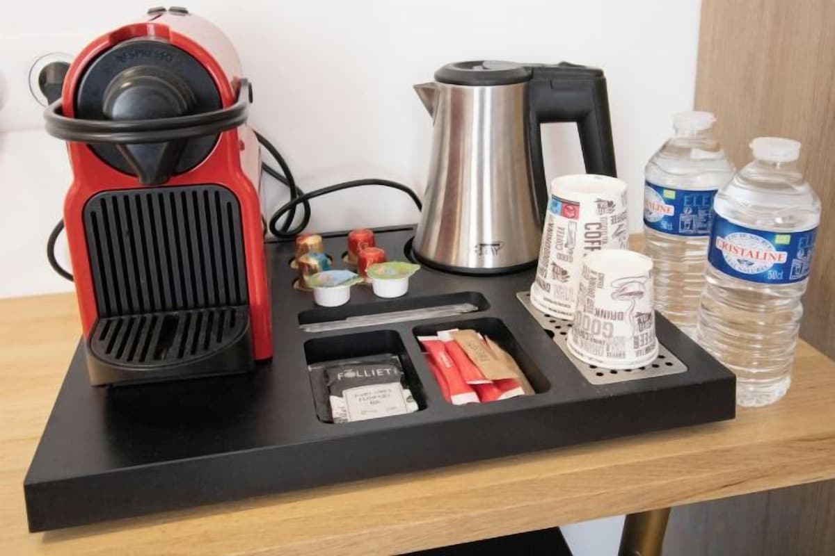 A coffee maker, a kettle, a coffee cup, a water bottle, and a small container on a black tray.