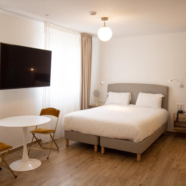 A hotel room with a bed, a television, a round table with a chair, and a window with curtains. - Les Rebelles Hôtel (Paris)