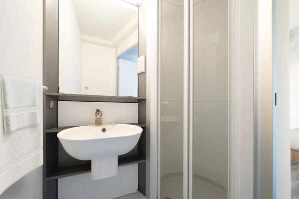 A modern bathroom with a white sink, a mirror, and a glass shower enclosure. - Student Only Chapter Islington in London (London)