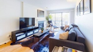 Een moderne woonkamer met een flatscreen televisie, een bank, een salontafel en een groot raam dat natuurlijk licht binnenlaat.
