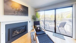 Een moderne woonkamer met een open haard, een groot raam met uitzicht, een gezellige zithoek en een decoratief kunstwerk.