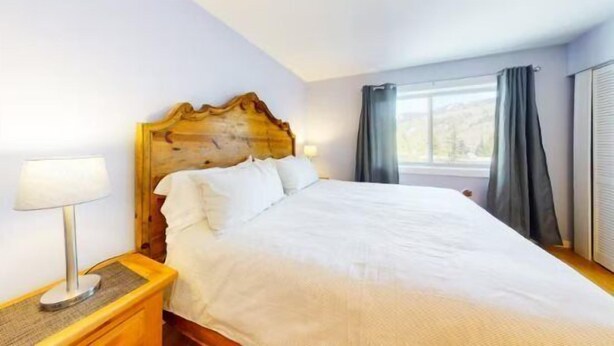 Een hotelkamer met een groot bed, een houten hoofdbord, een nachtkastje met een lamp en een raam met gordijnen.