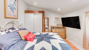 Une chambre à coucher avec un lit, un téléviseur fixé au mur, une commode et un miroir.