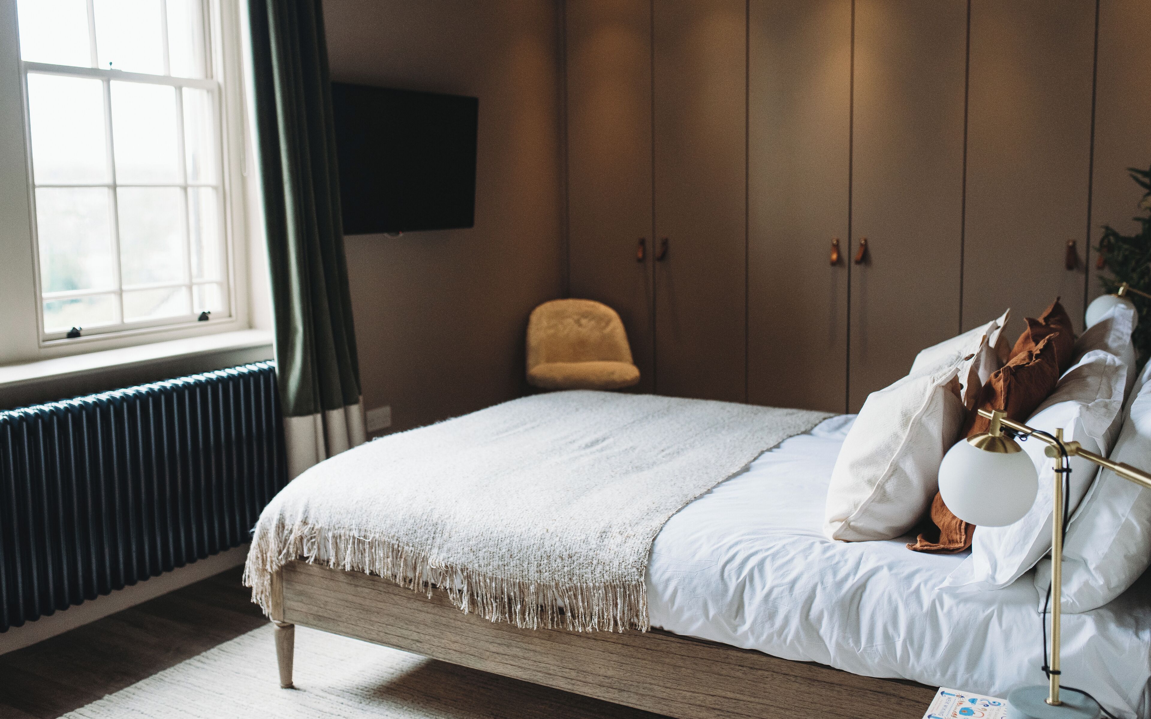 A bedroom with a bed, a chair, a radiator, and a TV on the wall.