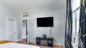 A bedroom with a bed, a TV mounted on the wall, a small console table with a plant, and a window with curtains. - Pet-friendly Stoughton Apartment w/ Outdoor Space (Stoughton)