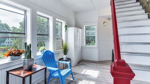 A room with a wooden floor, a blue chair, a small table, and a red staircase. - Pet-friendly Stoughton Apartment w/ Outdoor Space (Stoughton)