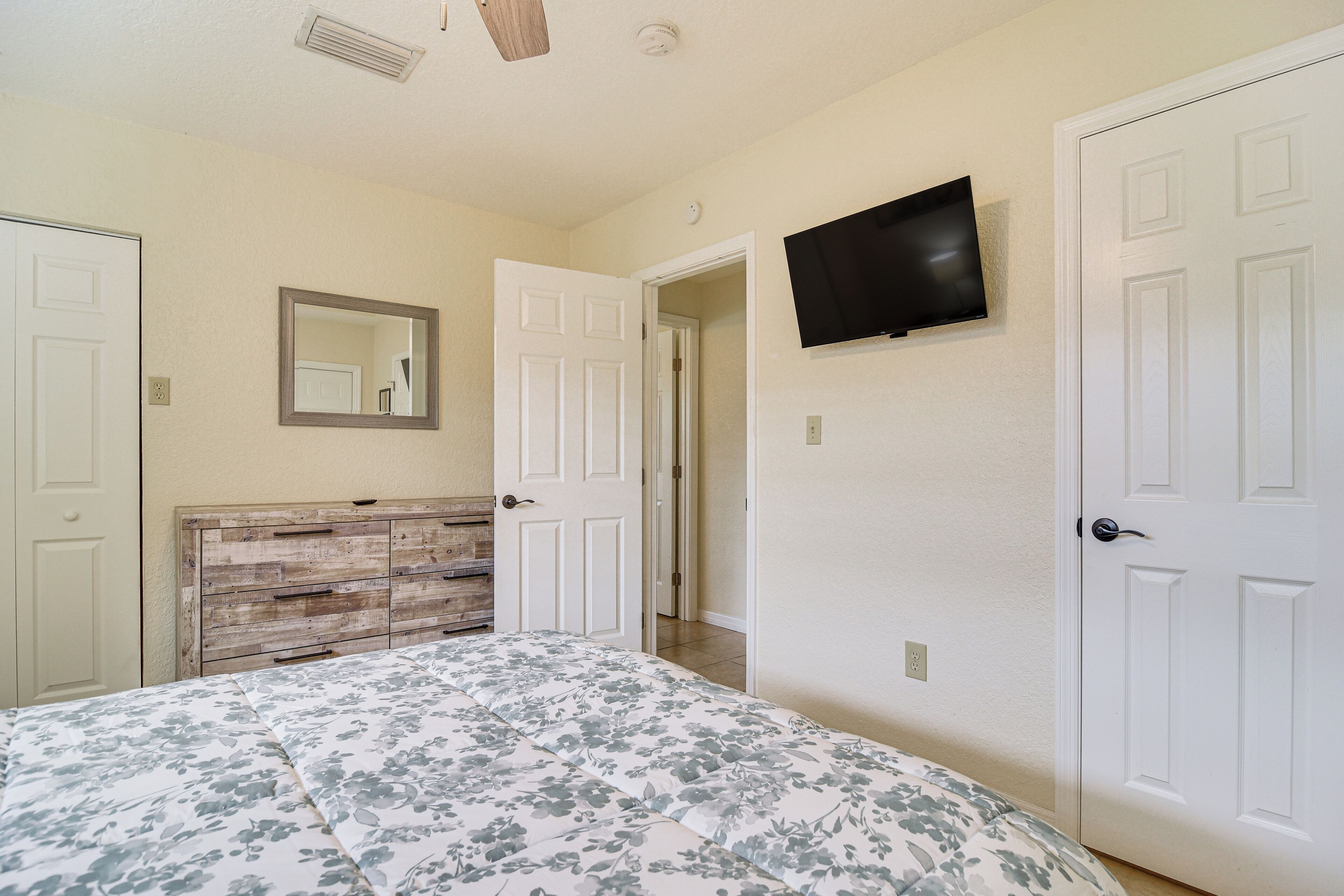 A bedroom with a wooden headboard, a bed with floral bedding, a mounted TV, and white doors.