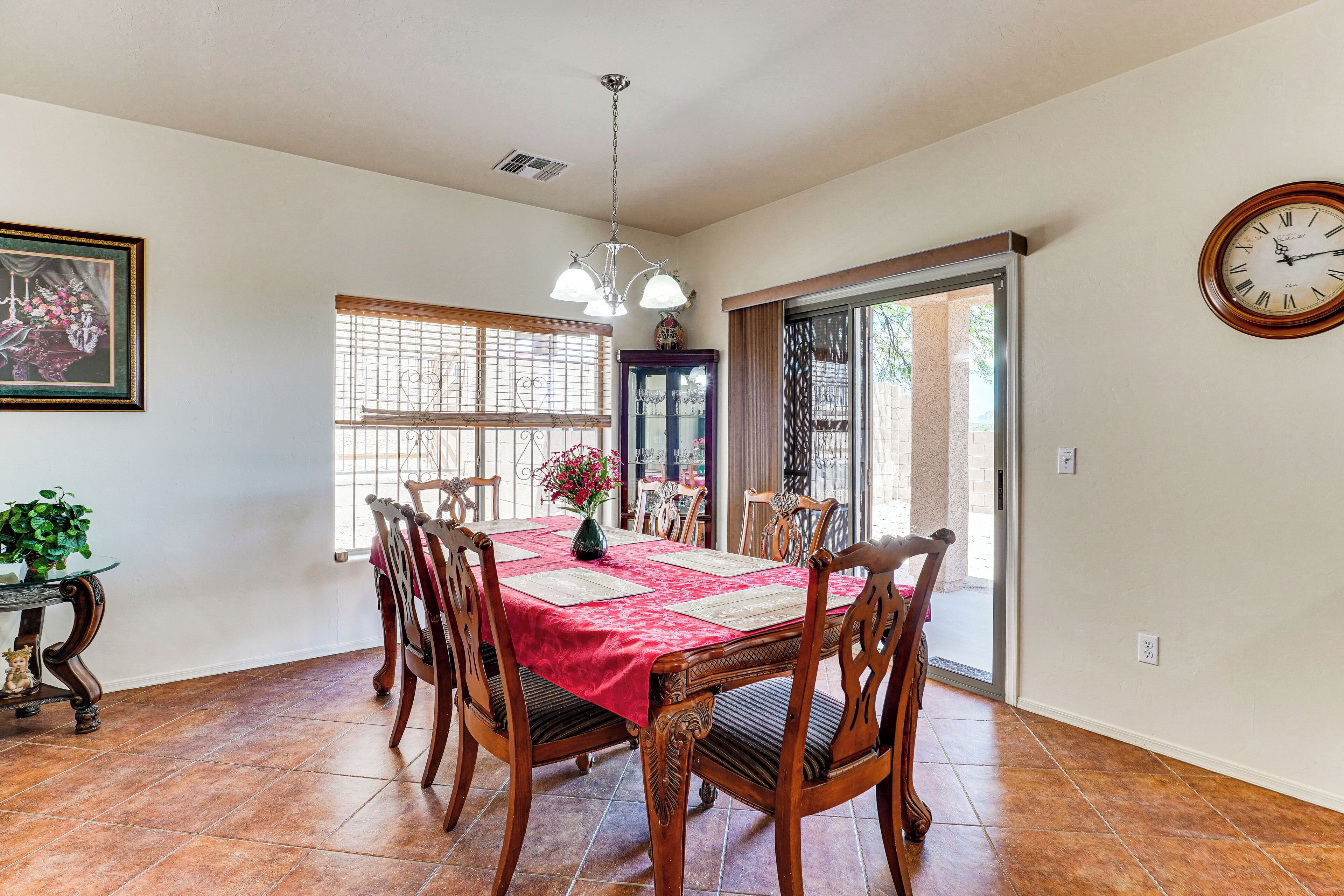 A dining area with a red tablecloth, wooden chairs, a chandelier, and a clock on the wall.