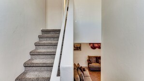 Eine Treppe mit Steinstufen und weißen Geländern führt zu einem Wohnbereich mit einer Couch und einem Bild an der Wand.