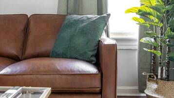 A brown leather sofa with a green pillow, a glass coffee table, and a large green plant in a woven basket.