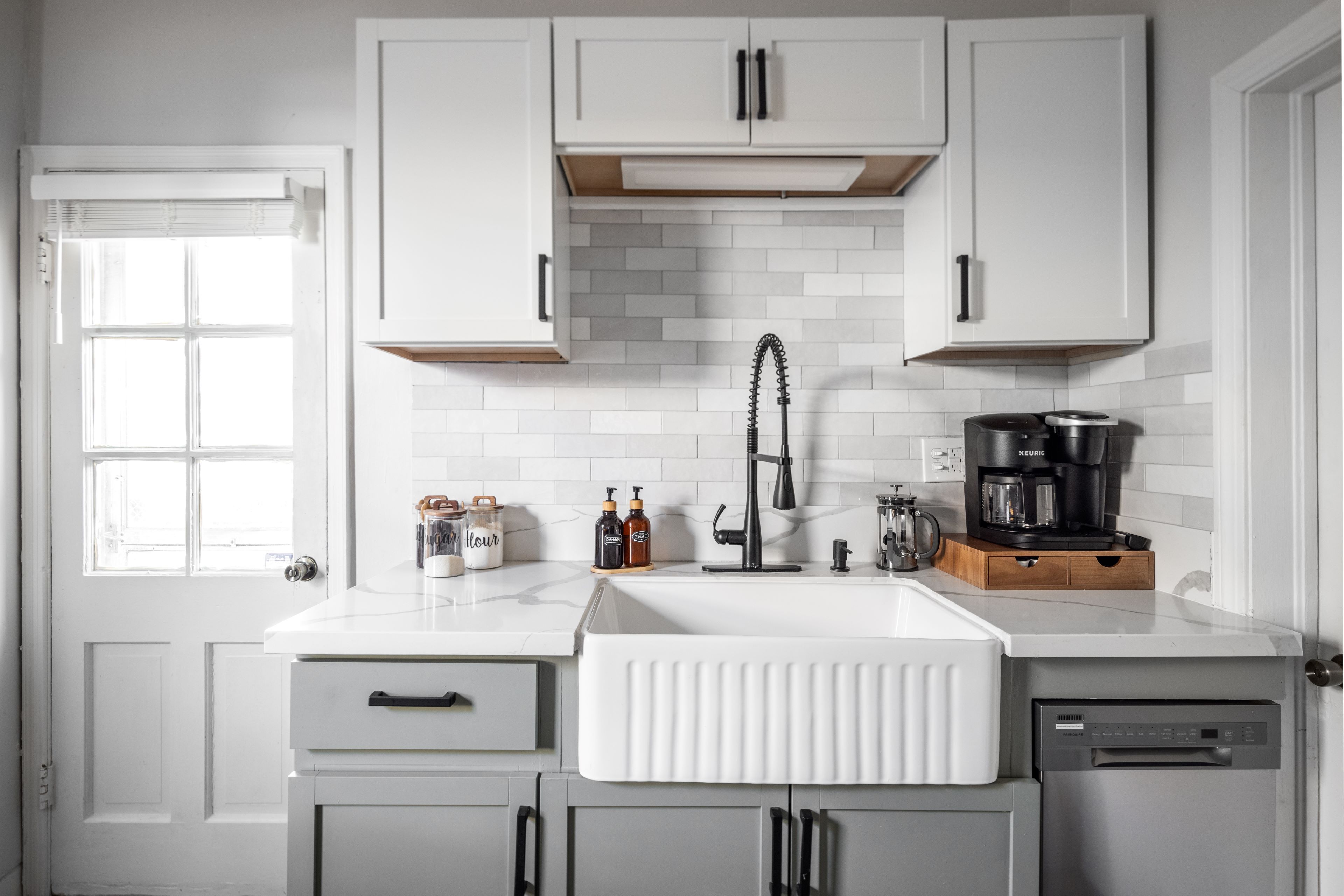A modern kitchen with white cabinets, a white countertop, a built-in dishwasher, and a coffee maker.