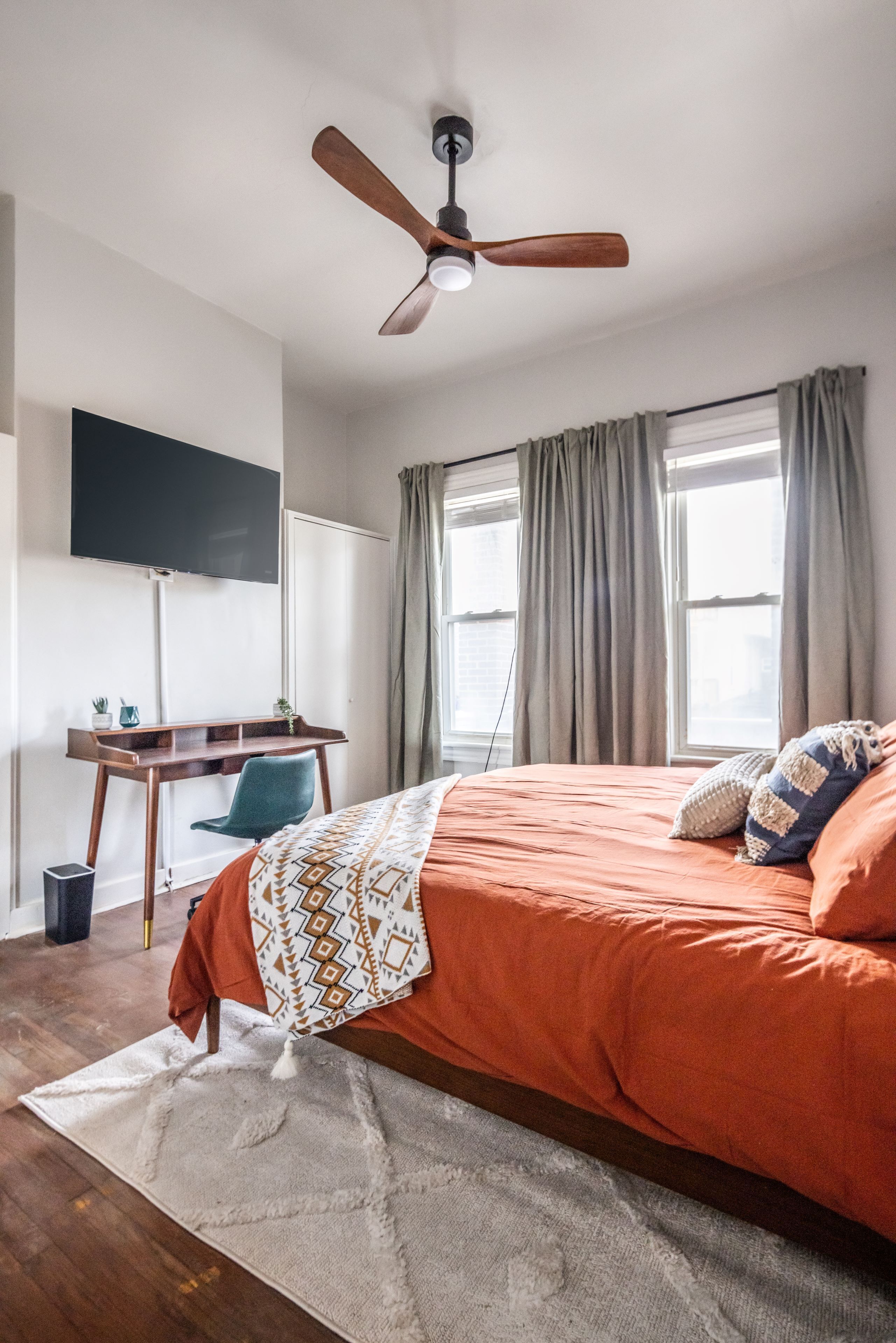 Ein Schlafzimmer mit Bett, Schreibtisch, Stuhl, Deckenventilator und einem an der Wand befestigten Fernseher.