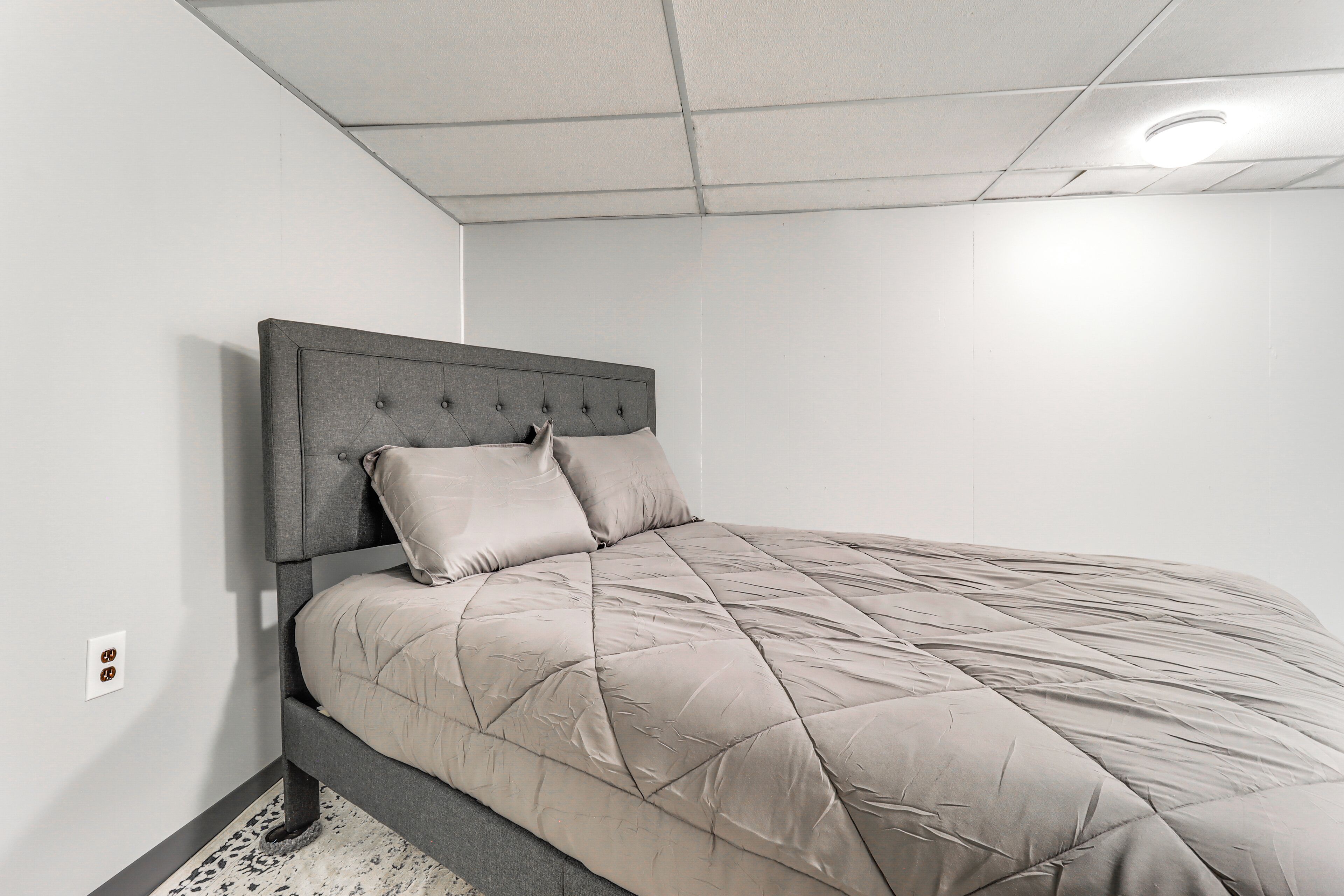 Een slaapkamer met een bed, hoofdeinde en een lichtschakelaar aan de muur.