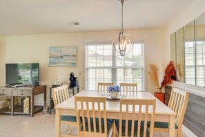 A dining area with a table, chairs, a chandelier, a painting, and a television. - Calabash Condo w/ Balcony in Gated Golf Community! (Calabash)