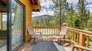 Puinen terassi, jossa on kaksi Adirondack-tyylistä tuolia, kuvioitu matto ja näkymä metsään ja vuorille.