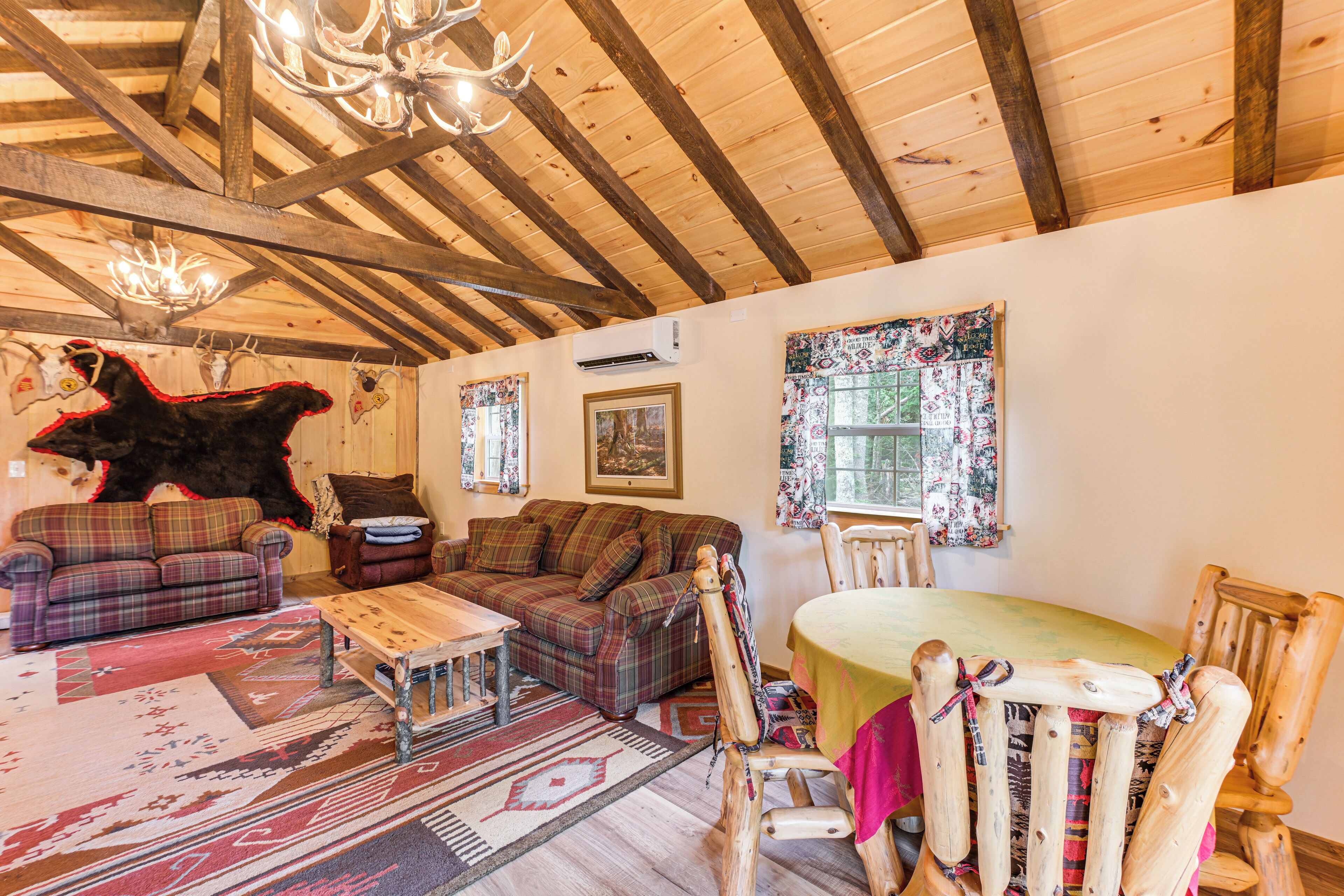Un interno rustico con travi in legno, un divano a quadri, un tavolo da pranzo in legno e un'ampia decorazione a testa di orso.