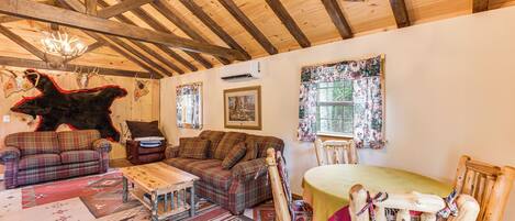 Un interno rustico con travi in legno, un divano a quadri, un tavolo da pranzo in legno e un'ampia decorazione a testa di orso.