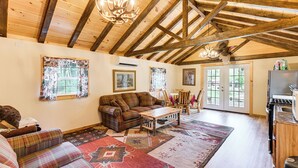 A cozy living room with a plaid sofa, a wooden coffee table, and a large rug. There is a kitchen area with a refrigerator and a stove. - Harrington Cabin w/ Grills - Near Beaches & Hiking (Harrington)
