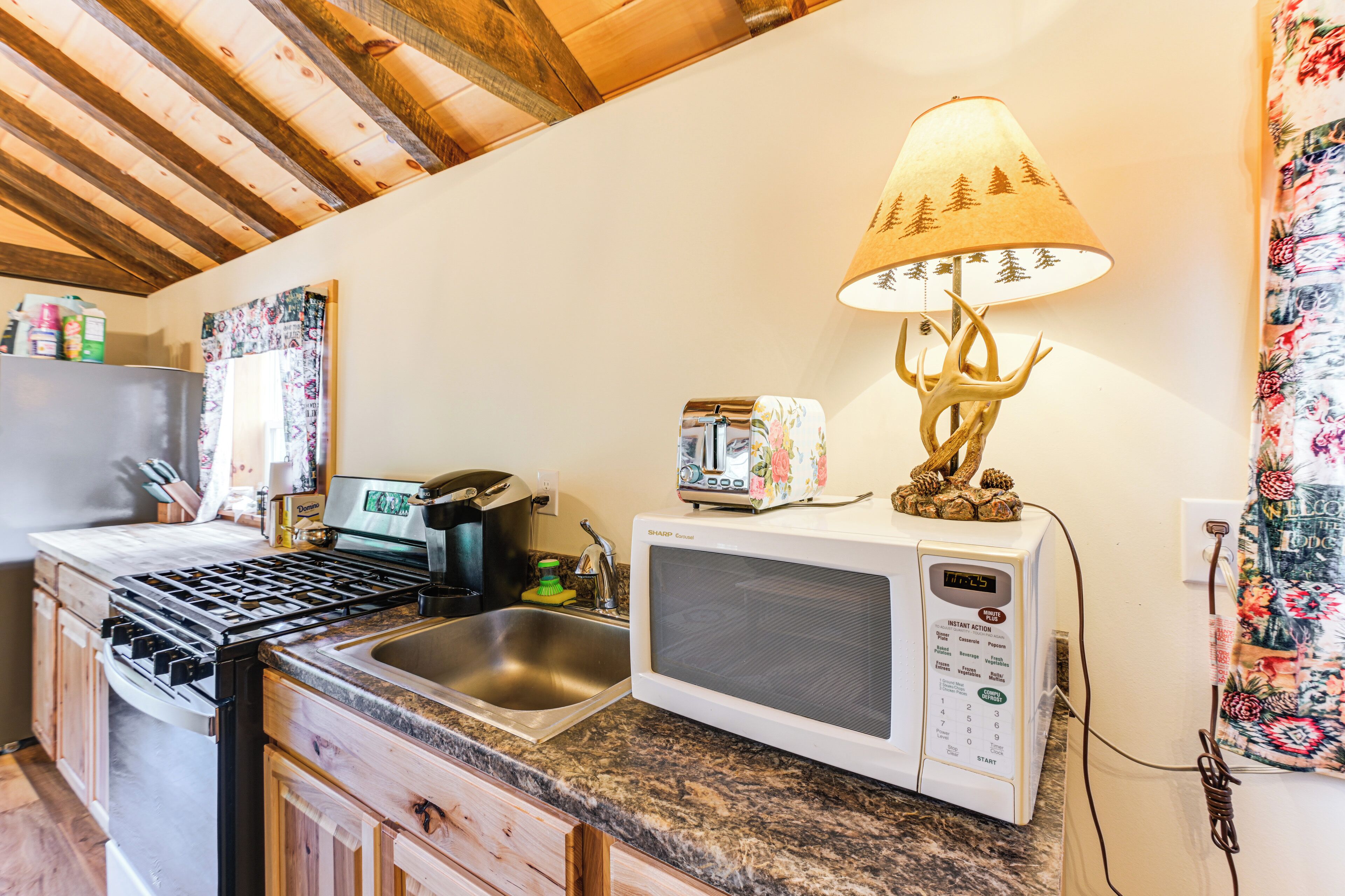 Una cucina con piano cottura a gas, forno a microonde, lavello e una lampada decorativa.