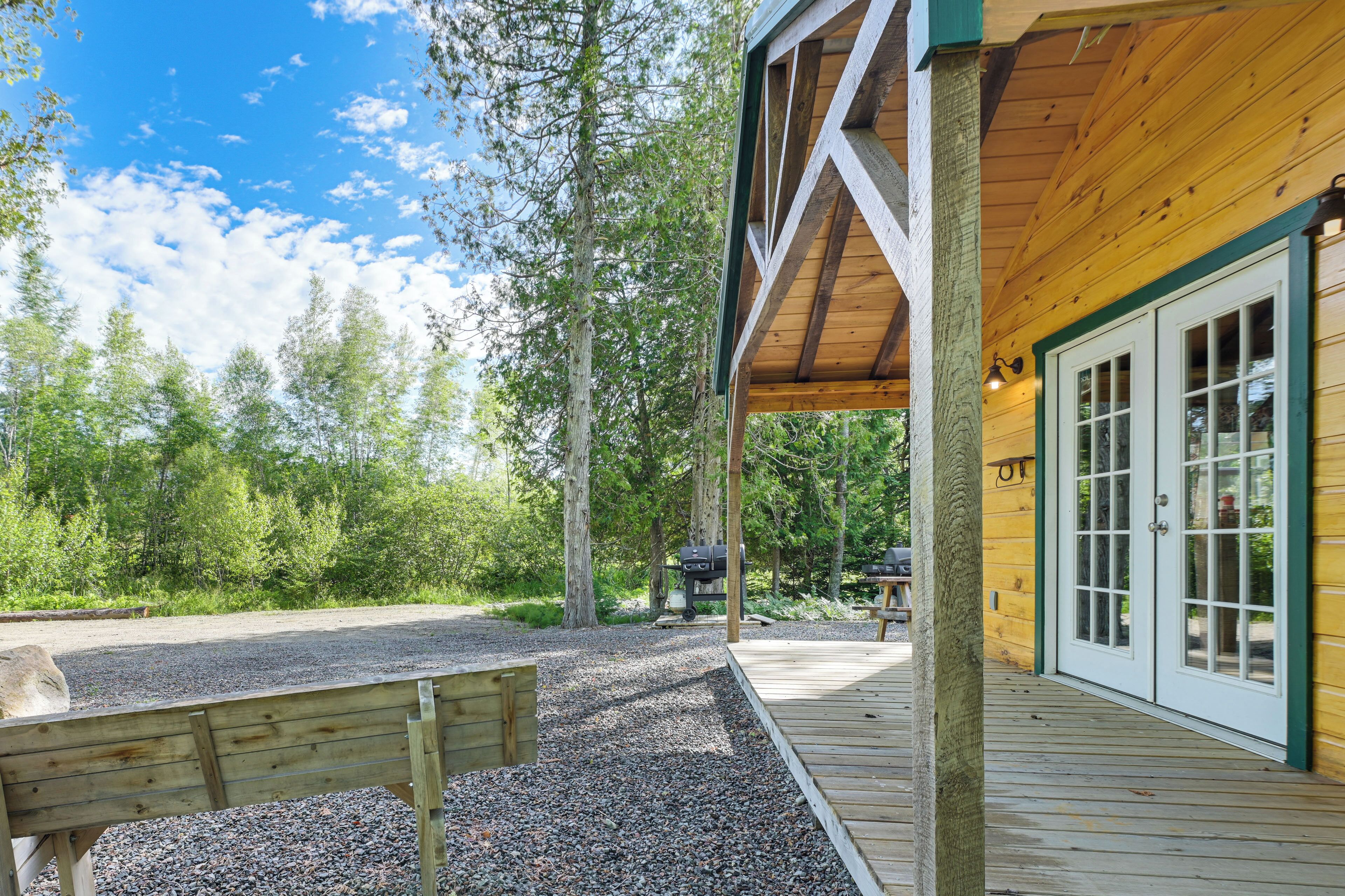 A wooden deck with a gravel path leading to a covered area with a grill and a bench.