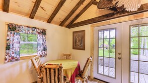 A rustic dining area with a wooden table and chairs, a patterned window treatment, and a door leading outside. - Harrington Cabin w/ Grills - Near Beaches & Hiking (Harrington)