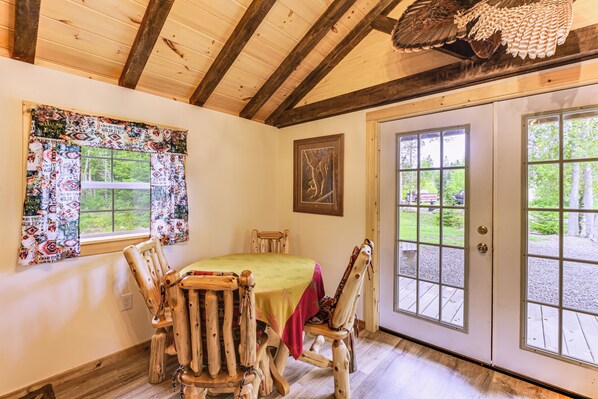 A rustic dining area with a wooden table and chairs, a patterned window treatment, and a door leading outside. - Harrington Cabin w/ Grills - Near Beaches & Hiking (Harrington)