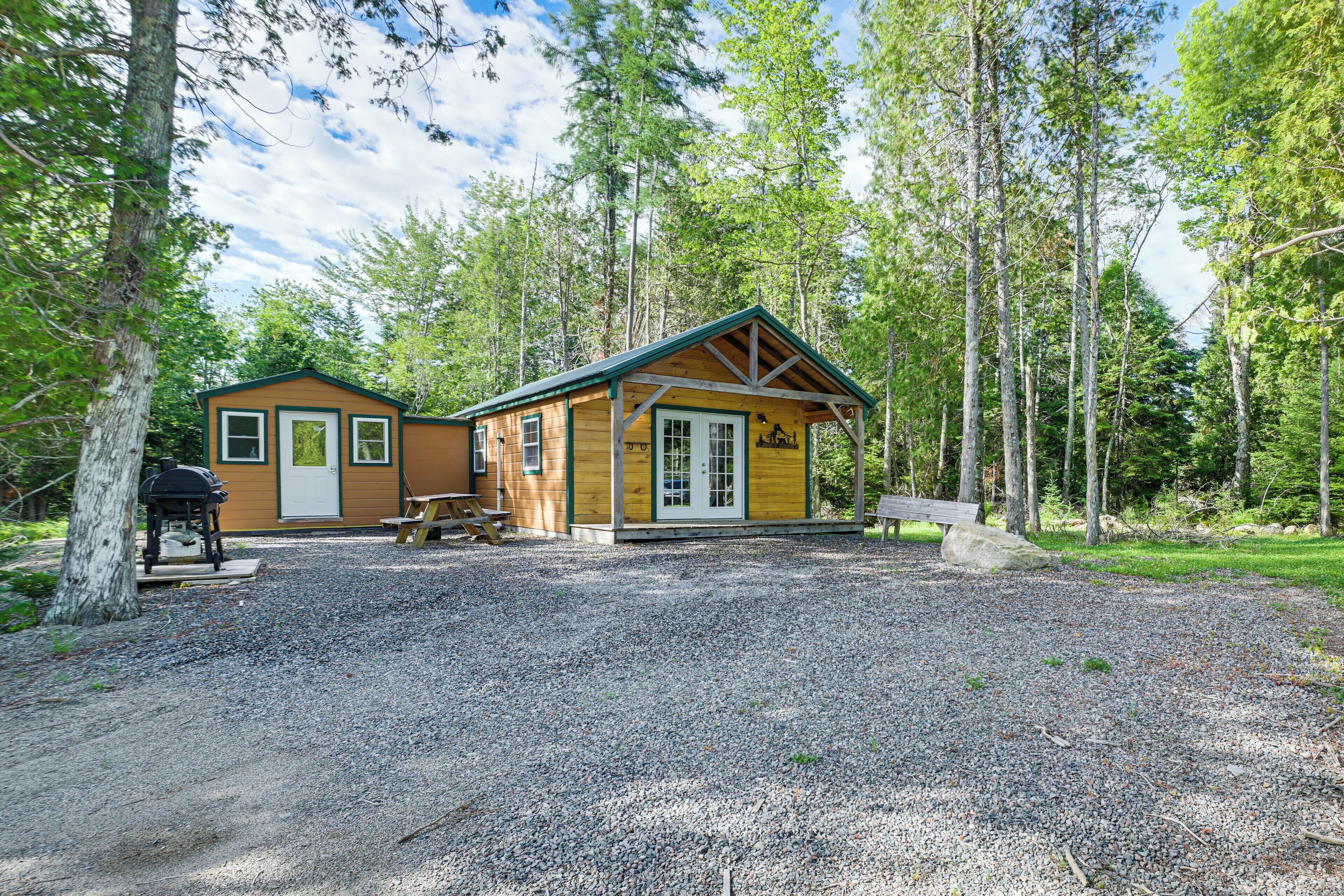 Une cabane avec une allée en gravier, une table de pique-nique et un barbecue.