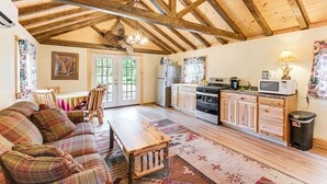 A spacious living room with a wooden ceiling, a plaid sofa, a dining table, and a kitchen area with wooden cabinets and appliances. - Harrington Cabin w/ Grills - Near Beaches & Hiking (Harrington)