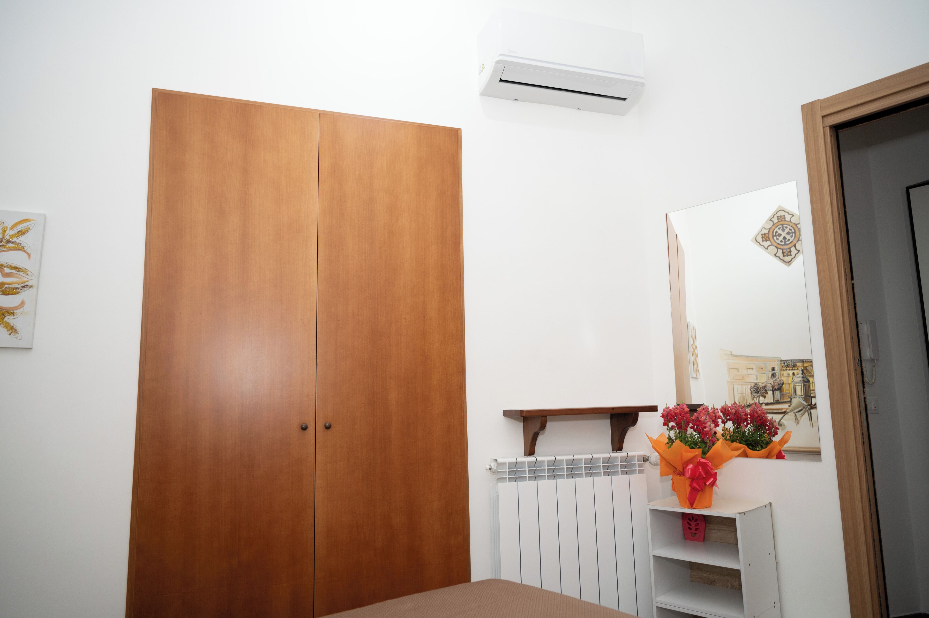 A room with a wooden wardrobe, a radiator, a mirror, and a small table with a bouquet of flowers.