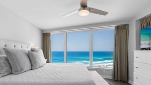 A bedroom with a large bed, a ceiling fan, a window with a view of the ocean, and a white dresser. - Update 2Br Beachfront Condo - Balcony View, Pool,  and Tram. Steps to Beach! (Miramar Beach)