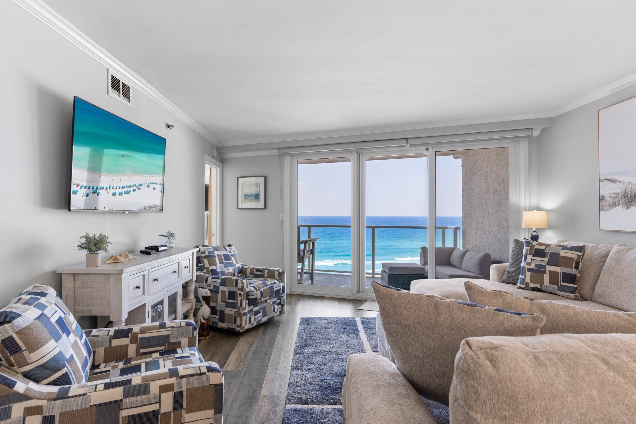 A living room with a view of the ocean, a large painting, and a white console table with decorative pillows.