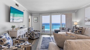 A living room with a view of the ocean, a large painting, and a white console table with decorative pillows. - Update 2Br Beachfront Condo - Balcony View, Pool,  and Tram. Steps to Beach! (Miramar Beach)