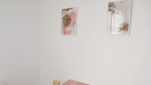 Une chambre avec un lit blanc, des coussins roses, un plaid rose et deux œuvres d’art murales.