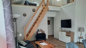 A modern living room with a staircase, a sofa, a coffee table, and a TV. - Ankerplatz in Idyllischer Umgebung und Nähe zum Bernsteinsee (Wiefelstede)